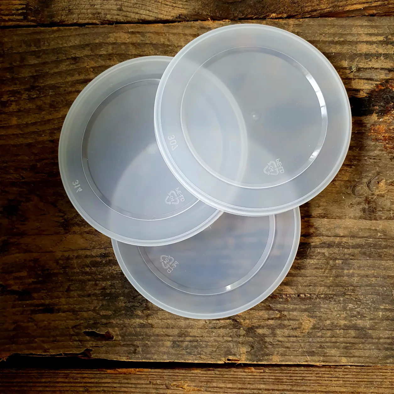 Drei transparente Kunststoffdeckel für Tierfutterdosen auf rustikalem Holzuntergrund